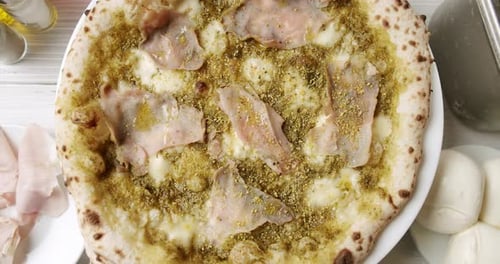 Top View of Tasty Italian Pizza with Ham Cheese and Pesto on Spinning Plate