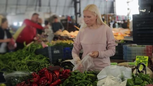 A Pretty Woman is Shopping at Market Picking Up Red Pepper in a Plastic Bag