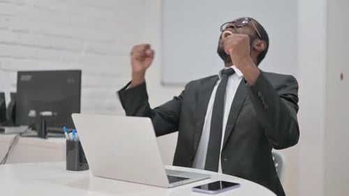 Excited Man Celebrating Success at Laptop in Office