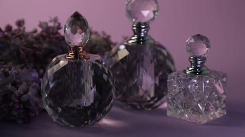 Perfume bottles and beautiful lilac flowers on violet background, closeup. Changing direction