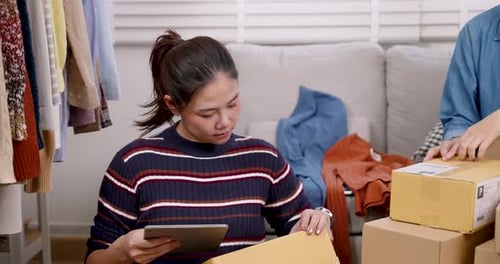 Asian woman online seller holding parcel box with one hand, reviewing shipping information on