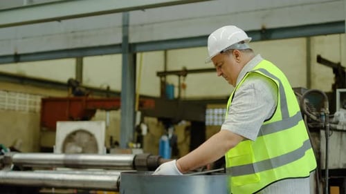 senior male factory engineer uses a metal rod to inspect or adjust heavy machinery in an industrial