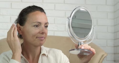 Woman Examines Face in Handheld Mirror Indoors