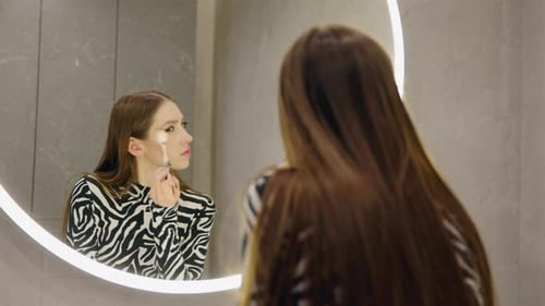 Woman Applies Makeup in Mirror in Modern Bathroom