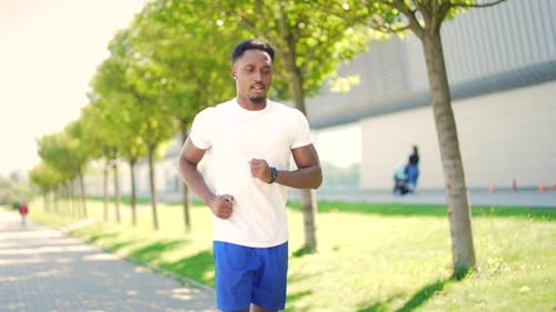 young African American man runner down the street on urban background of city park. Morning jog. Act