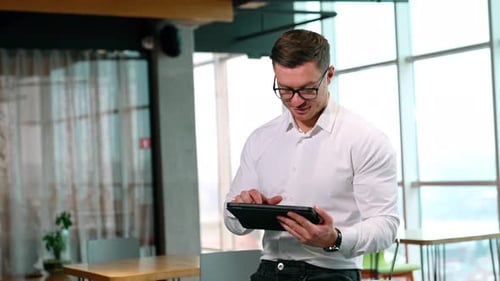 Using digital technology in modern business. Man in glasses works on his I-pad in a spacious office.