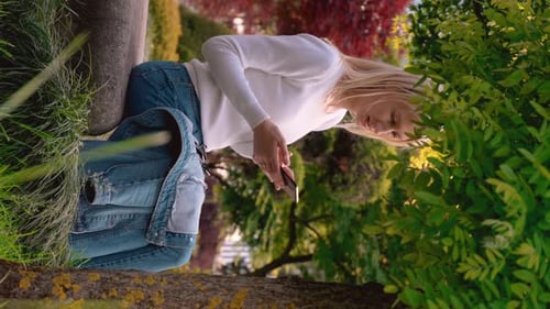 Young woman sitting in meadow in park and looking at her phone