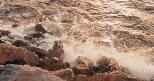 Waves Break on Rocky Shore of Sea at Sunset Time