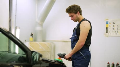 Muscular Auto Mechanic Worker Using Grinding Unit to Polish Black Hood at Automobile Repair and
