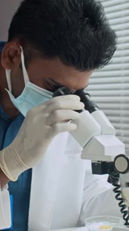Wissenschaftler mit Maske schaut durchs Mikroskop