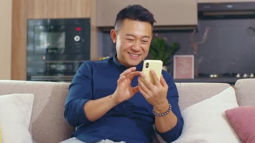 Happy Man Using Smartphone on Sofa at Home