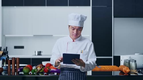 Asian Man Chef Using A Tablet In Home Kitchen