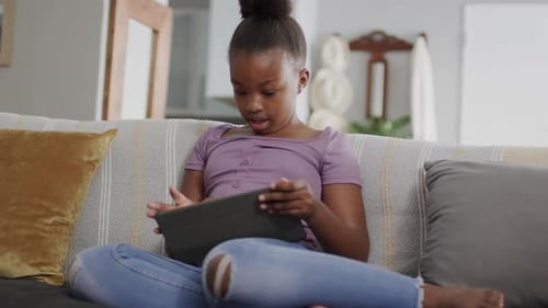 African american girl sitting on sofa and using tablet, slow motion