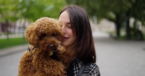 Smiling Woman Cuddling Toy Poodle in City Park