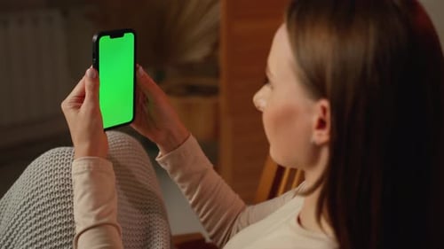 Closeup of a Woman Watching and Using a Smartphone on a Green Screen in the Living Room of the House