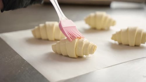 Chef Brushing Raw Croissants with Egg Wash in Bakery