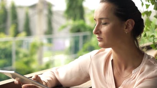 Woman With Tablet Computer Drinking Coffee In Cafe