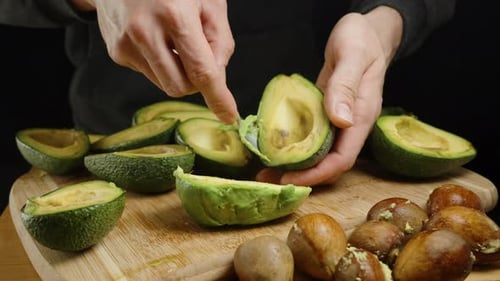Hands scooping avocado with spoon on cutting board