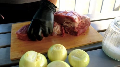 Gloved hand cuts raw meat on wooden board