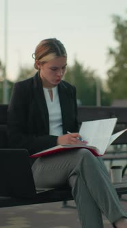 Focused young woman reviews documents on park bench