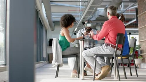 African american businessman wearing vr headset, gesturing while colleagues watching him at office