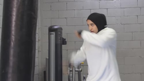 Strong Muslim Woman Prepares for Training Beats a Punching Bag Alone in the Gym