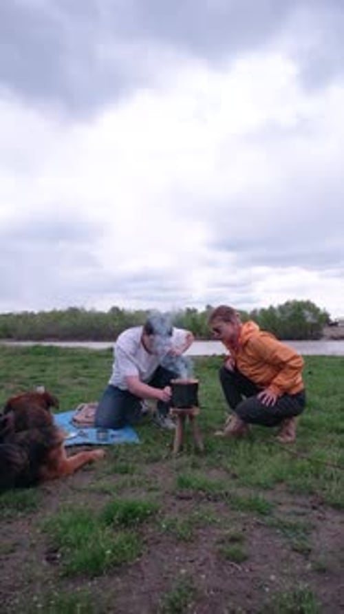 Family on picnic near the river cooking sausages on camping portable wood stove