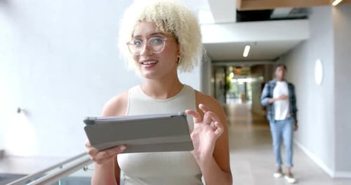 Using tablet, woman walking in modern office hallway, focusing on screen