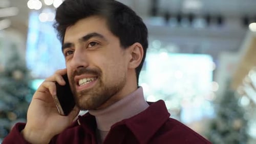 Closeup Face of Positive Bearded Young Man Talking on Mobile Phone Standing in Hall of Celebrate