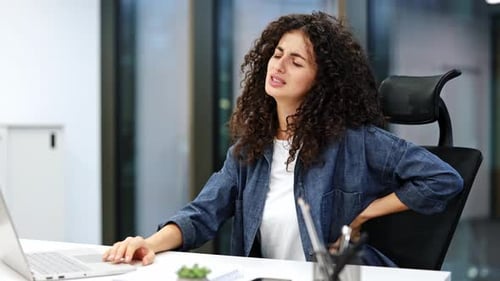 Businesswoman with Back Pain in Office While Working at Desk