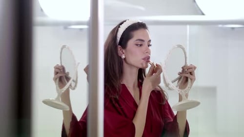 Woman Applies Lipstick with Hand Mirrors in Bathroom
