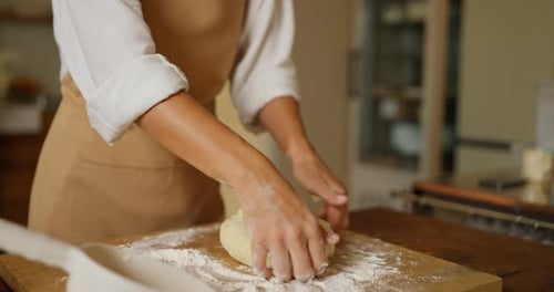 Girl Baker in a White Shirt and Beige Apron Kneading Dough on a Cutting Board Using Flour in a