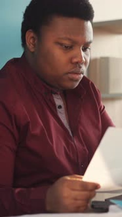 A Man Who is Wearing a Maroon Shirt is Reading a Document Closely