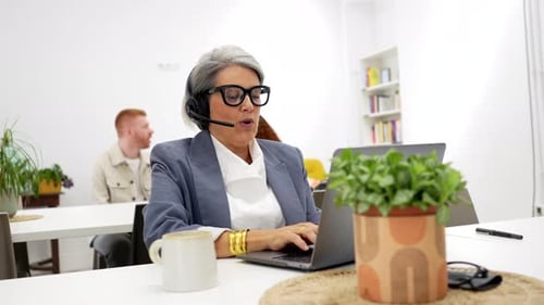 Senior Businesswoman Using Headset in a Busy Coworking Office Space