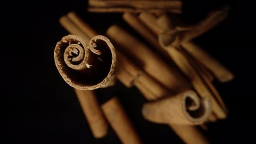 Scattered cinnamon sticks top view, one stick rotates, close-up.