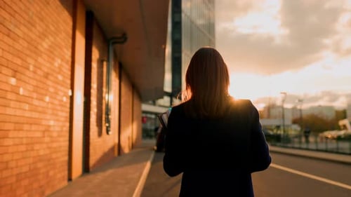 Woman Walks in City at Sunset with Laptop