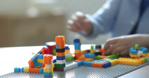Konstruktionsspielzeug Kleiner Junge spielt drinnen mit Bausteinen am weißen Tisch, Nahaufnahme