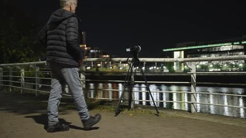 Camera tripod equipment, mature male photographer, city waterfront, night