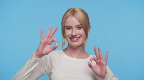 Smiling Woman Gives OK Hand Gesture on Blue