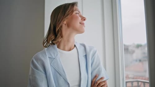 Smiling Woman in Pajamas Stands by Apartment Window