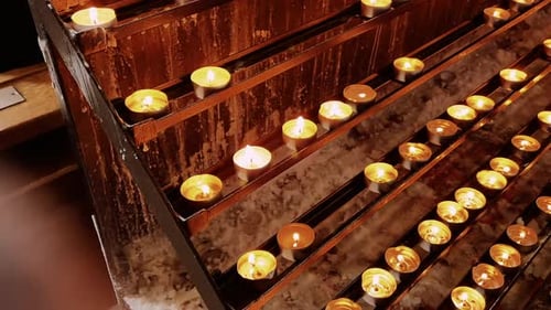 Golden candlelight flickers on a brown metal stand filled with melted white wax