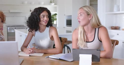 Diverses femmes collaborant à table dans la cuisine, la femme de droite proposant la femme au centre écrivant des notes