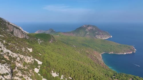 Türkisfarbenes Wasser funkelt unter der Sonne, während eine Kamera an einem sonnigen Tag über üppig grüne Berge schwenkt