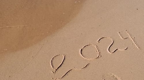 New Year Concept Text 2024 Handwritten in Sand Surface Blue Ocean Wave Washing Away Numbers at the