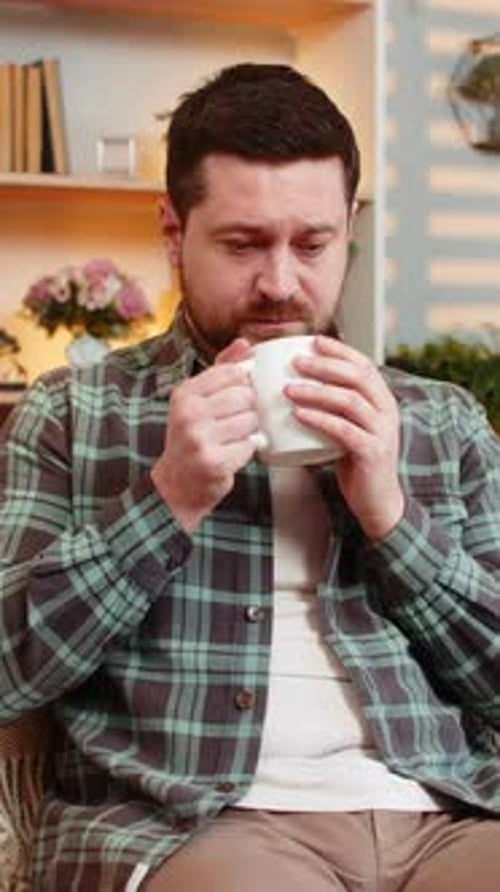 Young Man on Home Sofa Holding Coffee and Thinking Sadly About Work Life and Hard Decision Indoors