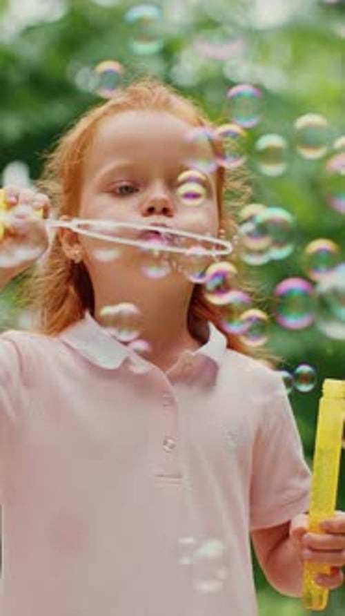 Young Girl Blows Bubbles in a Park Surrounded By Greenery on a Sunny Day