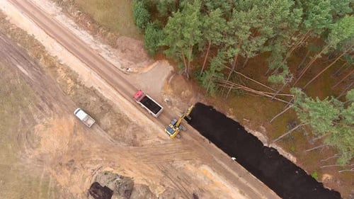 Dump truck and heavy digger constructing gravel road, aerial view