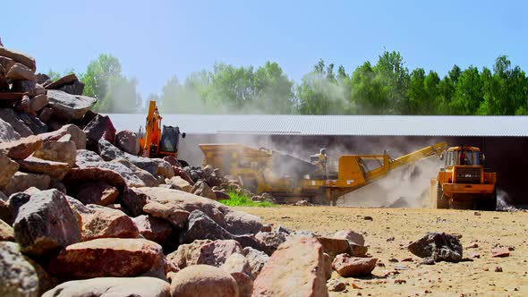 Excavator loading aggregate material in a rock crusher to pulverize ...