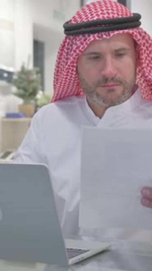 Man Works on Laptop with Documents in Office