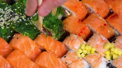 Japanese kitchen with sea food. Putting one sushi roll from set using sticks for sushi. Hand hold
